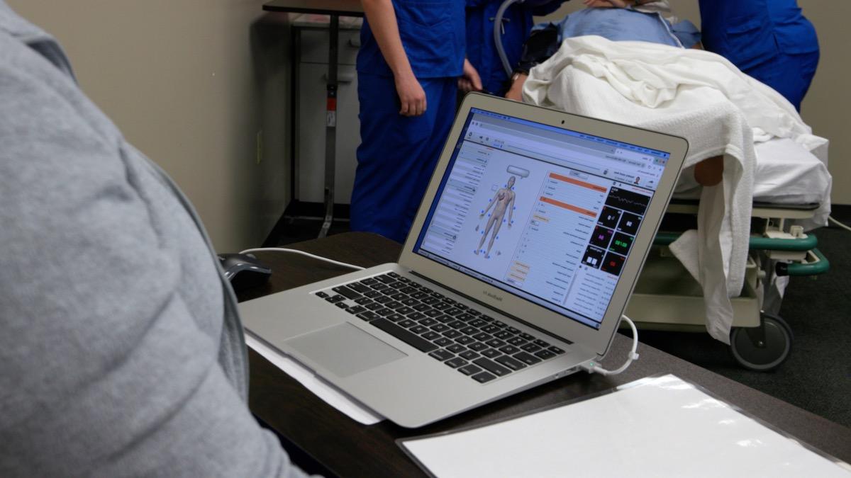 An informatics nurse working at a computer in front of a patient's hospital bed.